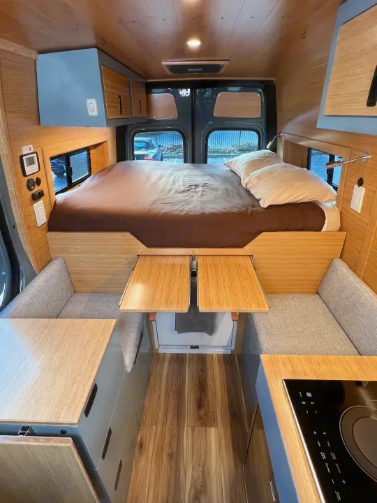 Spacious rv rental interior: bed, cozy seating with pull-out tables, integrated kitchen, and overhead storage.. Mercedes-Benz Sprinter 2024
