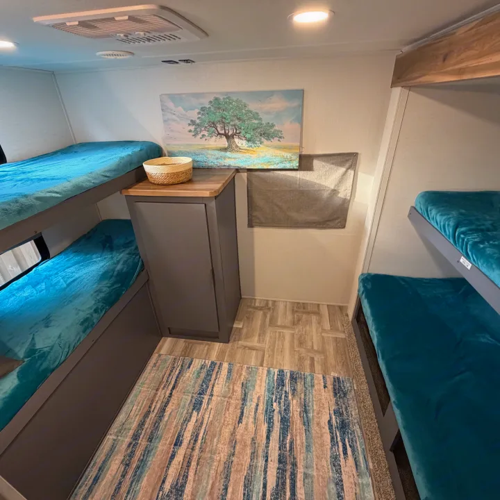 Spacious RV rental bunk room with four teal bunk beds, storage, and art. Ideal for family adventures.. Forest River Tracer Ultra Lite LE 2025