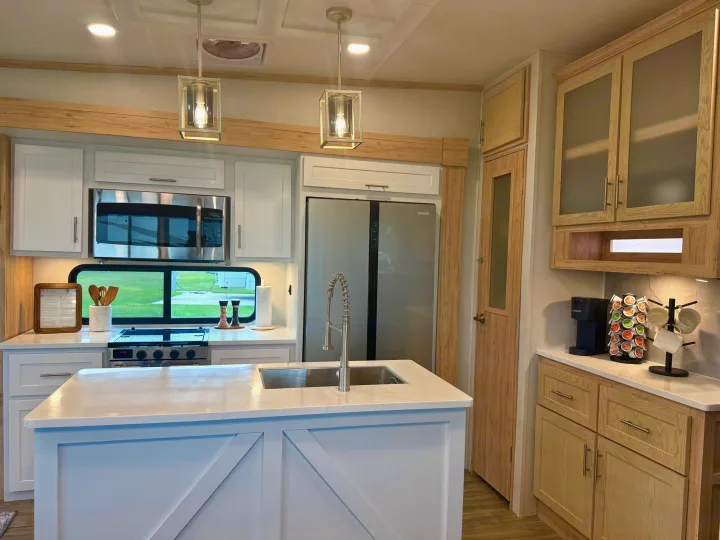 Experience a stylish RV rental! This modern kitchen features white cabinets, an island, and stainless steel appliances.. Alliance RV Avenue 2023