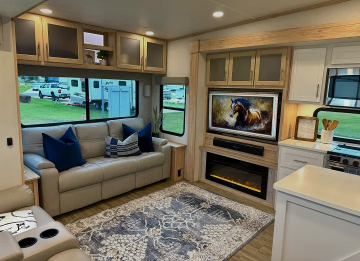 This modern RV rental features a cozy living area with a fireplace, TV, kitchenette, light wood cabinetry, and outdoor views.. Alliance RV Avenue 2023