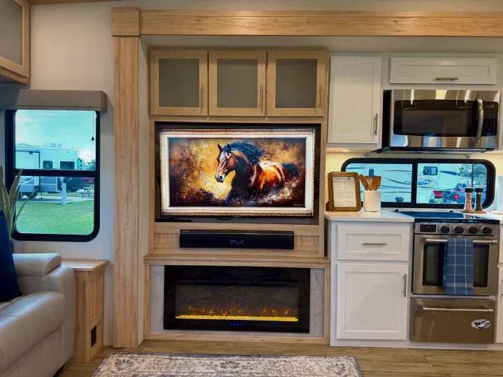 Stylish rv rental interior: TV over fireplace, full kitchen, and a window view of other campers parked outside.. Alliance RV Avenue 2023