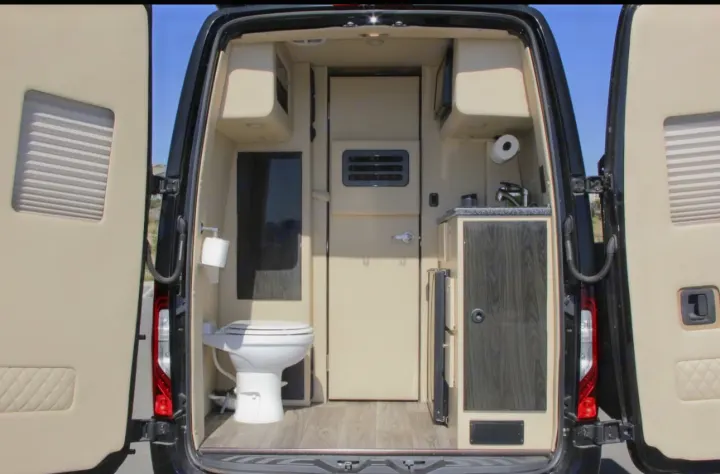 **RV rental**'s rear interior with open doors reveals a toilet, sink, and compact kitchen. Beige and dark wood design.. Ultimate Toys Ultimate Presidential 2020