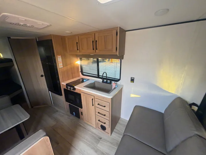 This modern RV rental features a functional kitchen with a sink, stove, microwave, and fridge, plus dining and living space.. Keystone RV Coleman 2025