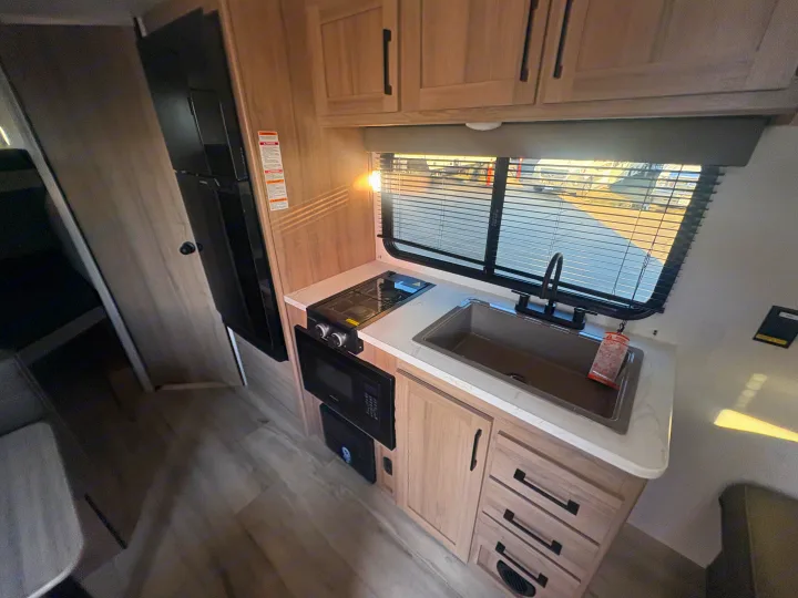 This rv rental features a modern kitchen with a sink, stove, microwave, and refrigerator, all complemented by light wood cabinets.. Keystone RV Coleman 2025