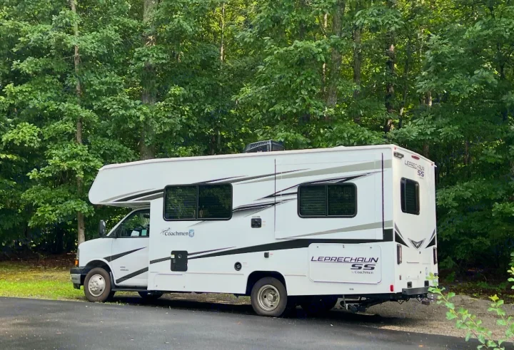 White Coachmen Leprechaun SS motorhome RV rental parked on asphalt with lush green trees in the background.. Coachman Leprechaun 2025