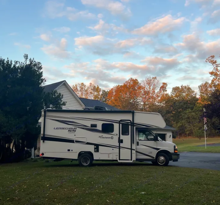 White Coachmen Leprechaun RV parked on a green lawn by a house. Perfect for your next rv rental adventure. A pristine motorhome.. Coachman Leprechaun 2025
