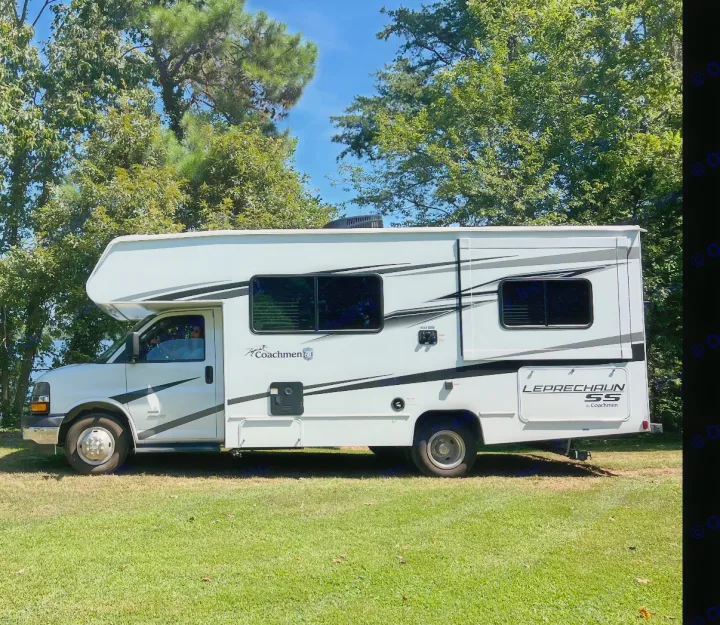White Coachmen Leprechaun SS motorhome, great for rv rental, parked on green grass against a backdrop of trees and blue sky.. Coachman Leprechaun 2025