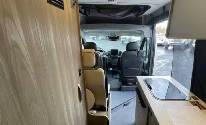 Interior view of an RV rental camper van, featuring a compact kitchen counter on the right and the front cabin seats ahead.. Winnebago Solis 2025
