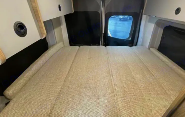Relax in this RV rental's cozy camper van interior: a segmented bed, overhead storage, and a rear window view.. Winnebago Solis 2025