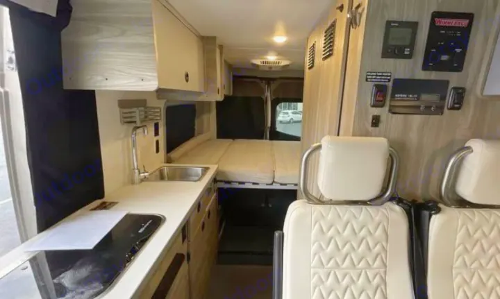RV rental interior featuring a kitchen with sink and stovetop, a convertible bed, and cream quilted seats.. Winnebago Solis 2025