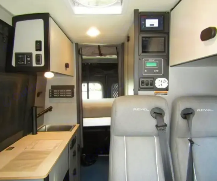 This RV rental interior features a compact kitchen with sink, integrated control panel, and two 'Revel' passenger seats.. Winnebago Revel 2025