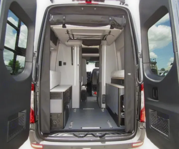 View from open rear doors into a grey camper van interior. Modular units, a central aisle, and overhead storage, ideal for an rv rental.. Winnebago Revel 2025