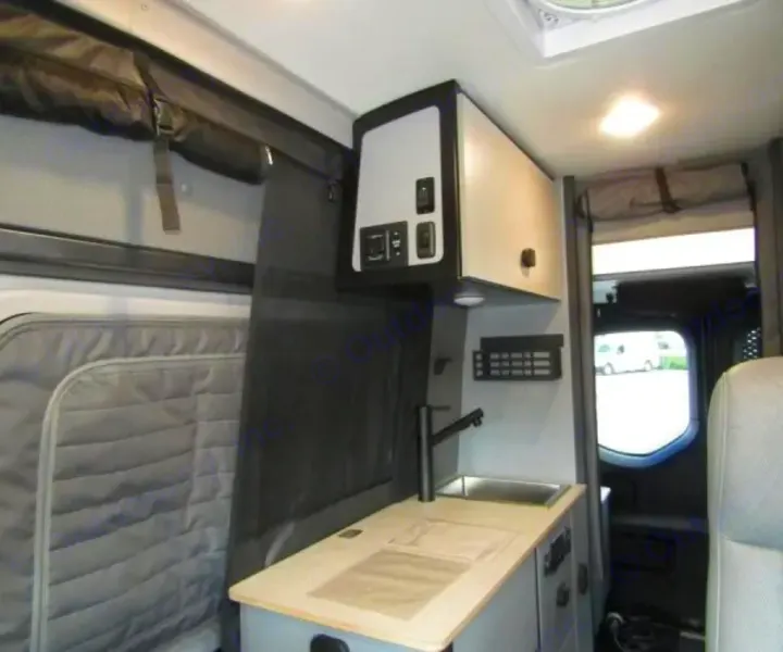 This RV rental's interior features a compact kitchen with a sink, overhead cabinet with controls, window covers, and a rear view.. Winnebago Revel 2025