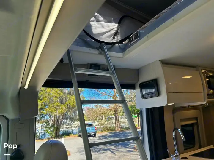 RV rental: Interior shows a ladder to a pop-top bed, control panel, kitchen sink, and a scenic outdoor view.. Thor Tellaro 2023