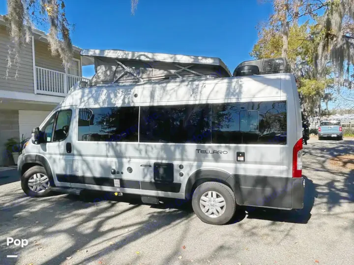 Stylish light grey Tellaro pop-top camper van, available for rv rental, parked on asphalt with tree shadows.. Thor Tellaro 2023