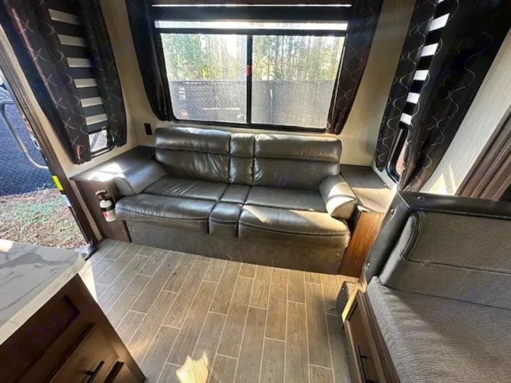 Spacious RV rental interior with a comfy sofa, wood-look floor, and windows. This camper offers a cozy living space.. Forest River Cherokee Grey Wolf 2020