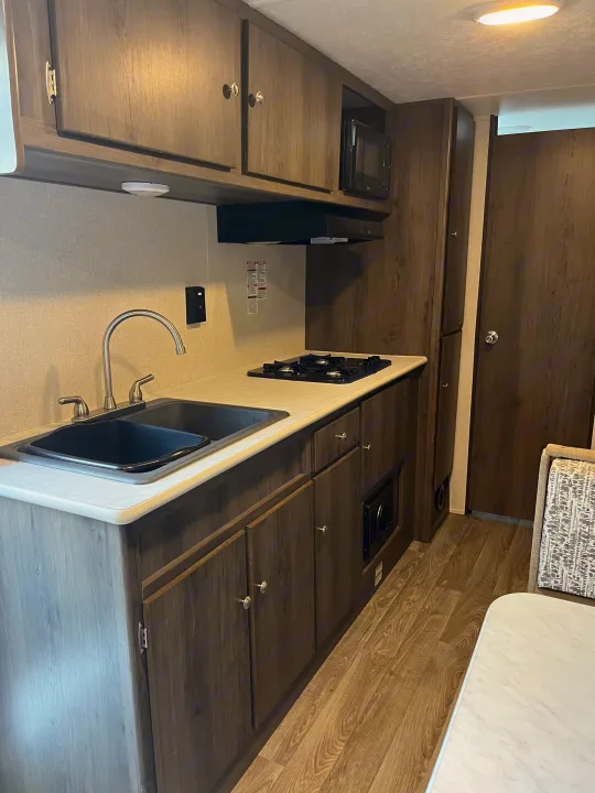 Modern RV rental kitchen featuring a double sink, gas stove, microwave, and dark wood cabinetry for convenient living.. Coachmen Viking Saga 21SBH 2019