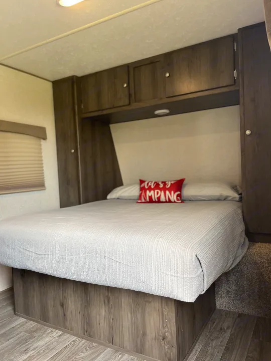 Cozy RV rental bedroom featuring a comfy bed, overhead cabinets, and a "Let's Go Camping" pillow. Perfect for your next adventure!. Coachmen Viking Saga 21SBH 2019