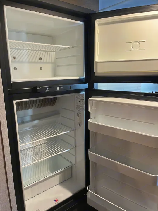 Empty, clean RV rental refrigerator and freezer. Both doors are open, revealing wire shelves and door bins.. Coachmen Viking Saga 21SBH 2019
