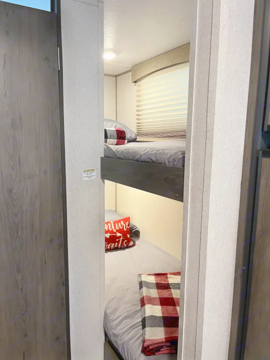 Inside an RV rental: clean, cozy bunk beds with plaid blankets & window blinds. A 300 lb weight limit is visible.. Coachmen Viking Saga 21SBH 2019