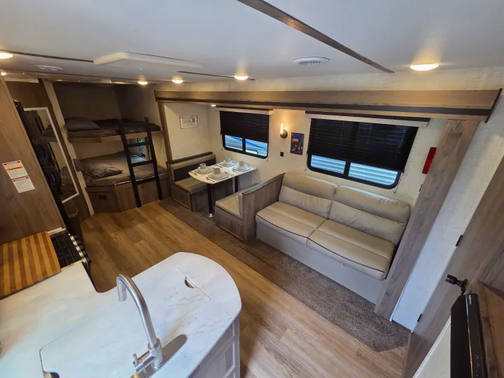 RV rental interior featuring a kitchen island, dining booth, sofa, and bunk beds, offering a complete living space.. Gulf Stream Kingsport 2022
