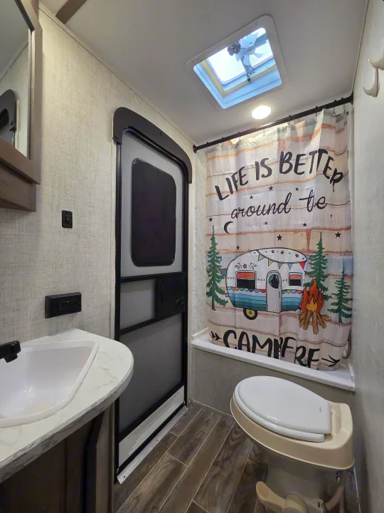 Inside an RV rental bathroom, featuring a sink, toilet, shower with a "campfire" curtain, and roof vent.. Gulf Stream Kingsport 2022