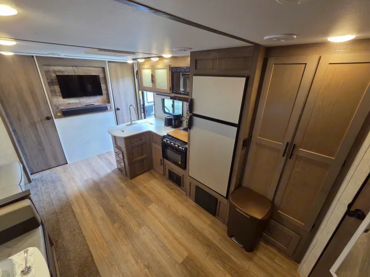 Bright rv rental living & kitchen area: sleek fridge, oven, microwave, sink, TV, and wood-grain cabinetry await your adventure.. Gulf Stream Kingsport 2022