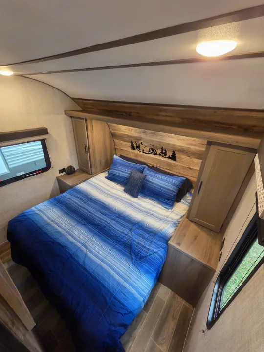 Cozy RV rental bedroom featuring a blue striped bed, wooden storage, overhead light, and a unique camper headboard.. Gulf Stream Kingsport 2022