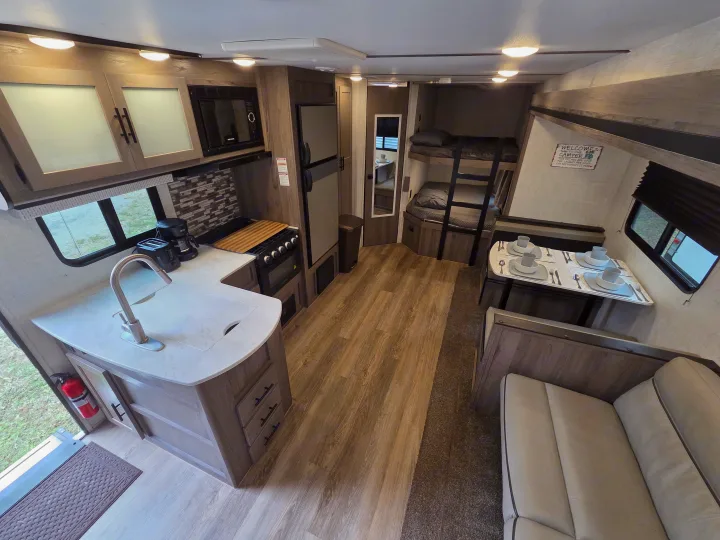 A bright RV rental interior featuring a kitchen, dining area with place settings, bunk beds, and a sofa. Perfect for travelers!. Gulf Stream Kingsport 2022