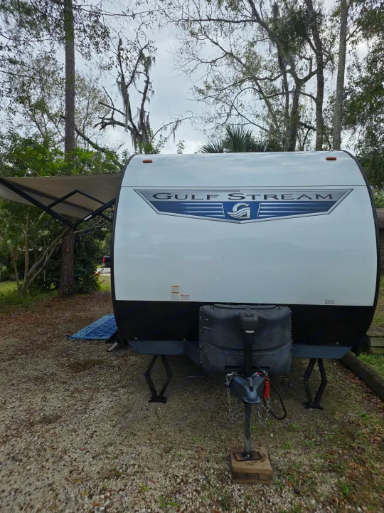 This Gulf Stream rv rental travel trailer is parked on gravel with an extended awning amidst trees, ready for adventure.. Gulf Stream Kingsport 2022