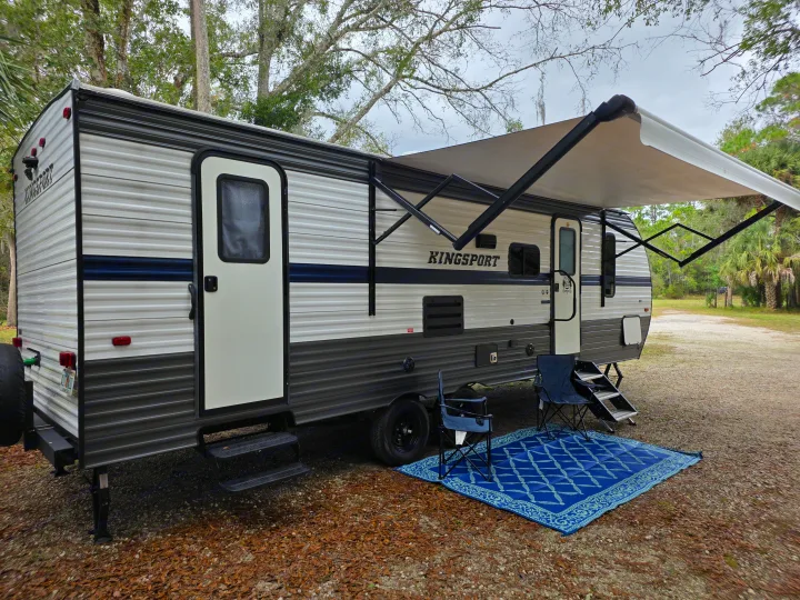 This Kingsport RV rental is ready for camping, featuring an extended awning, chairs, and a blue rug outside.. Gulf Stream Kingsport 2022