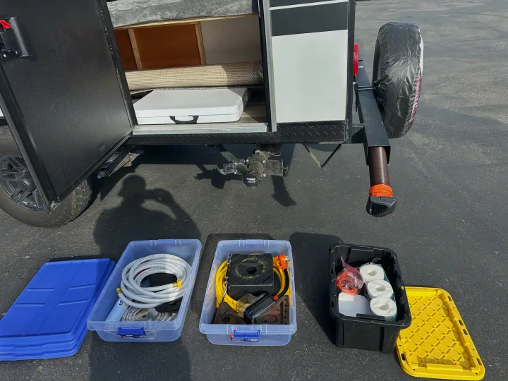 Prepping an RV rental: Open storage compartment, rug, table inside. Bins on ground hold hoses, power cord, TP for the journey.. Forest River Cherokee Wolf Pup 2023
