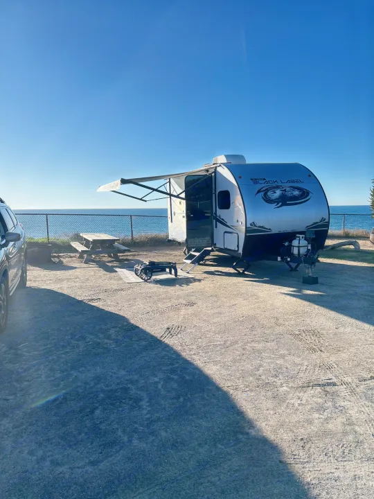 Scenic RV rental campsite by the ocean. A travel trailer, picnic table, and fire pit are set up for a perfect getaway.. Forest River Cherokee Wolf Pup 2023