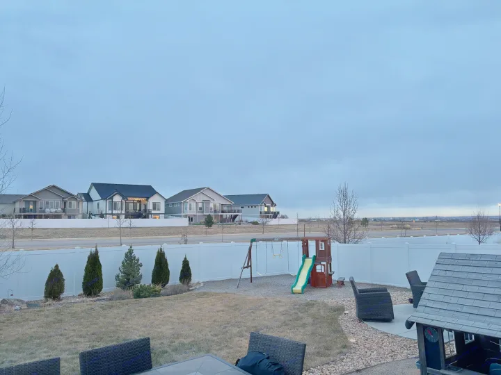 Suburban backyard with playset, patio, & houses beyond the fence under cloudy skies. Great for relaxing between RV rental trips.. Thor Four Winds 2023