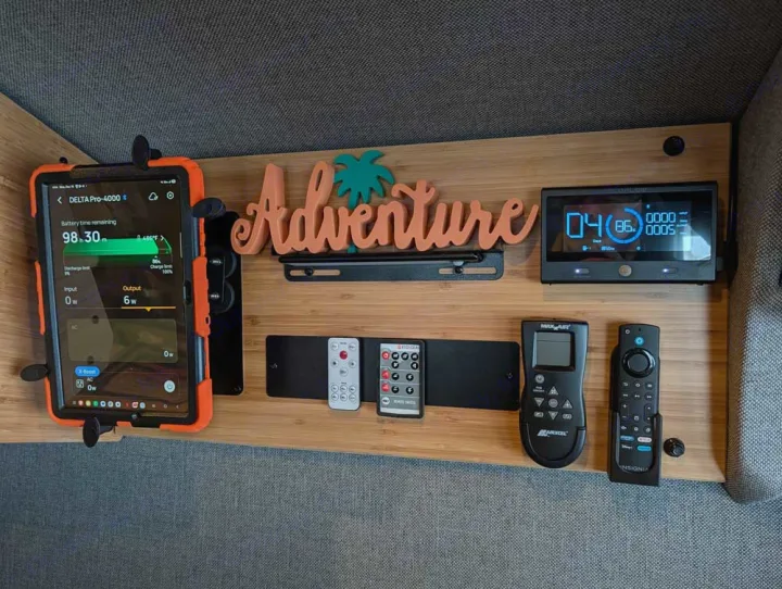 RV rental tech setup: Power station monitor (98.30m), control panel, "Adventure" sign, and remotes neatly on a wood panel.. Winnebago Adventure Wagon 2023