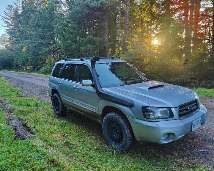 Beyond RV rental: This rugged silver Subaru Forester is ready for off-road forest exploration, parked on a dirt road at sunset.. Subaru Forester 2007