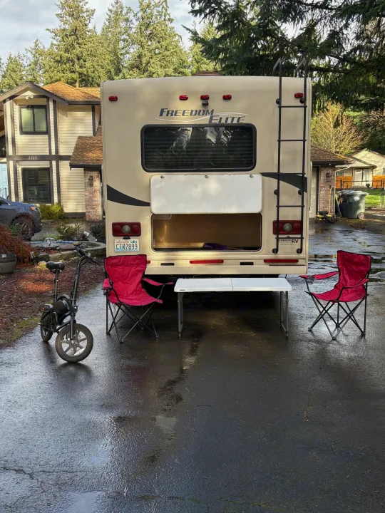 Freedom Elite RV rental parked with an outdoor setup: red chairs, white table, and an e-bike, ready for travel adventures.. Thor Freedom Elite 2014