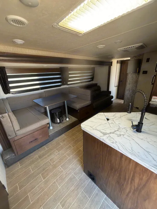 Modern RV rental interior featuring a gray dinette, sleek kitchen island with a marble countertop, and a comfortable living area.. Forest River Cherokee Grey Wolf 2021
