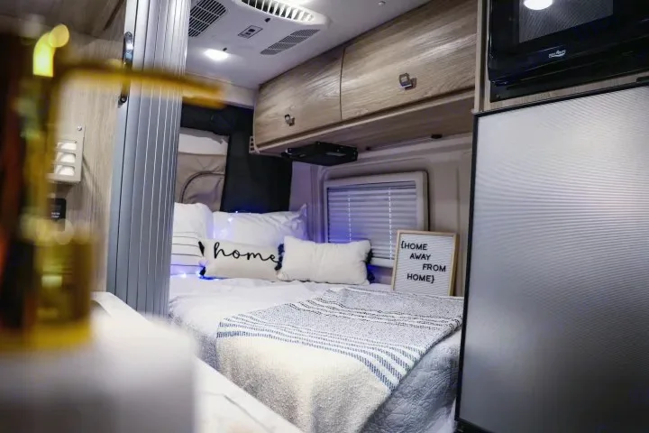 Cozy RV rental bedroom with "home away from home" sign, comfortable bed, string lights, and compact amenities.. Winnebago Travato 2022