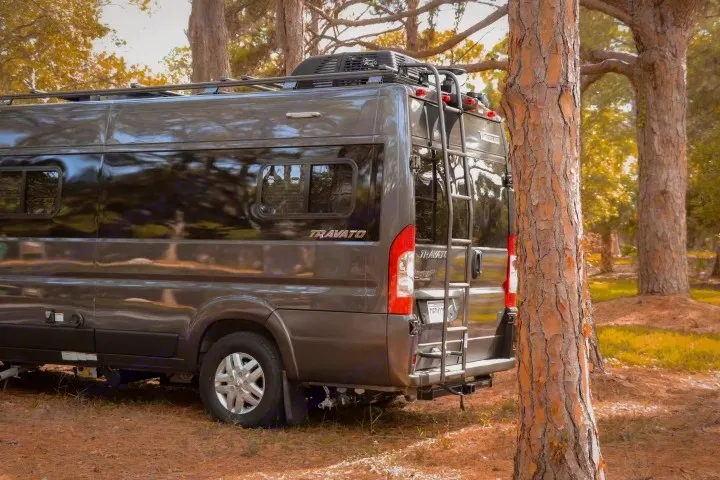 Dark grey Travato campervan parked in a peaceful forest setting, perfect for an RV rental adventure. Ready for the outdoors!. Winnebago Travato 2022