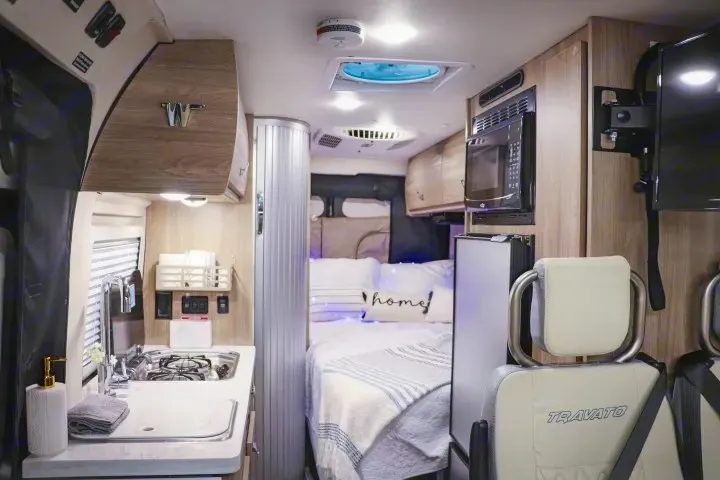 Compact RV rental interior with kitchenette, bed, microwave, fridge, and TV for comfortable travel.. Winnebago Travato 2022