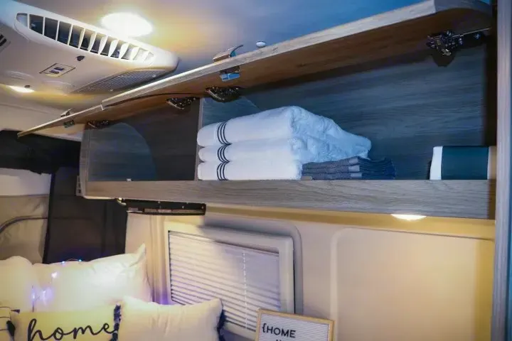 Cozy RV rental interior: open overhead storage, fresh towels, and AC for comfort on your journey.. Winnebago Travato 2022