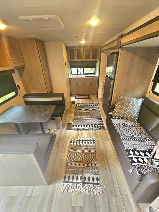 Bright RV rental interior: kitchen, dinette, and sofa with patterned rugs on light flooring. A welcoming, modern living space.. Keystone RV Springdale 2024