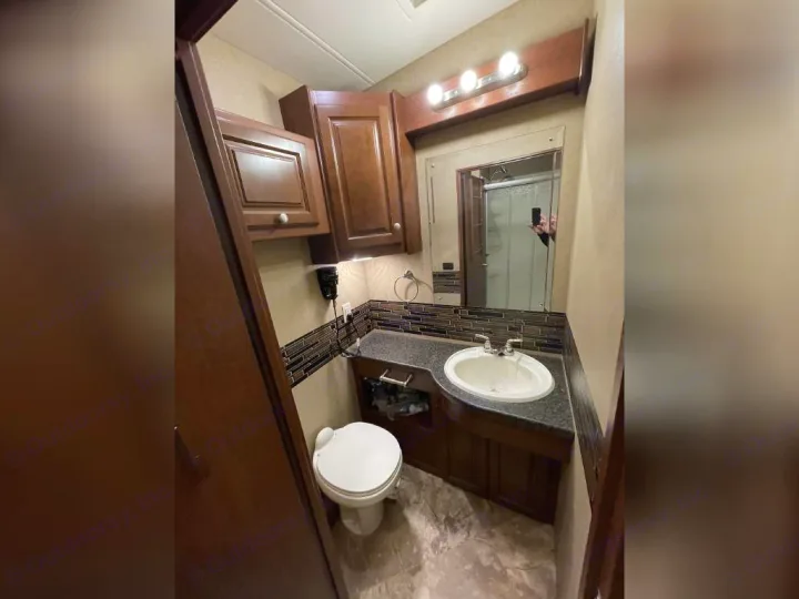 RV rental bathroom features dark wood cabinets, modern tile backsplash, sink, toilet, and vanity mirror with lighting.. Thor Outlaw 2017
