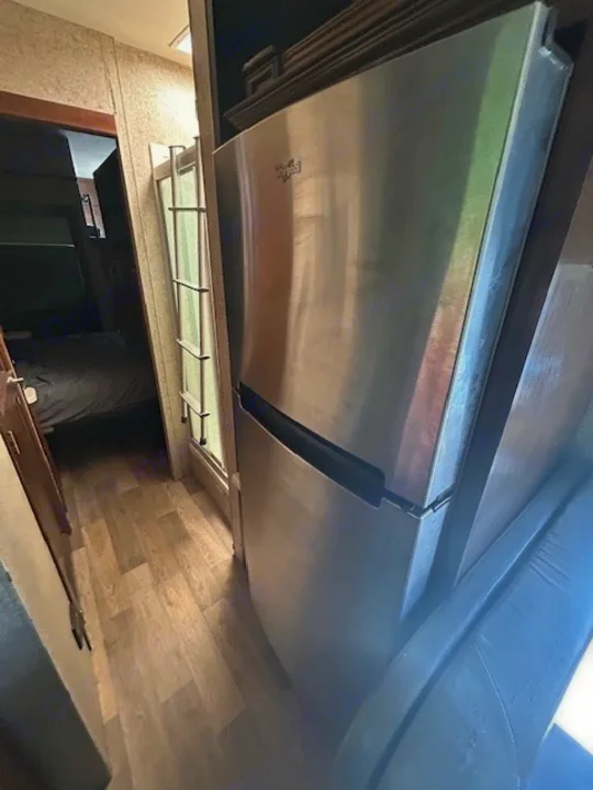 RV rental interior features: a sleek stainless Whirlpool refrigerator, wood-look floor, and a view into the bedroom.. Thor Outlaw 2017