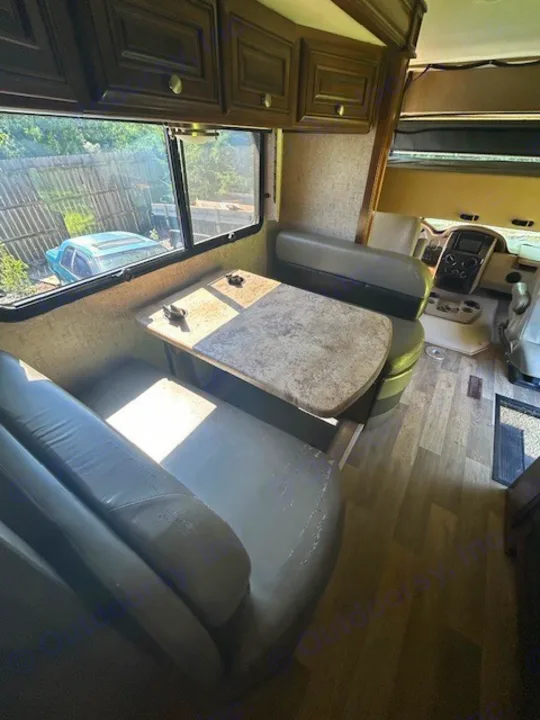 Spacious RV rental interior: dinette with light cushions, wood floor, overhead cabinets, and cockpit view.. Thor Outlaw 2017