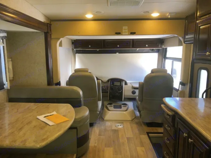 Spacious rv rental interior featuring a bright driver's cockpit, dining booth, and partial kitchen view with wood tones.. Thor Outlaw 2017