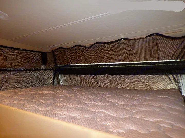Inside an RV rental: a cozy overhead bunk bed with a mattress and protective mesh safety nets for secure sleeping.. Thor Outlaw 2017