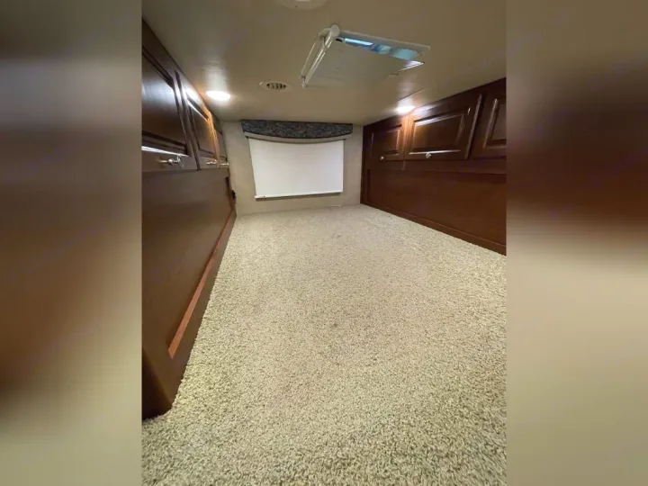 Inside an RV rental: a cozy bedroom or bunk space with light carpet, dark wood cabinetry, and a window blind.. Thor Outlaw 2017