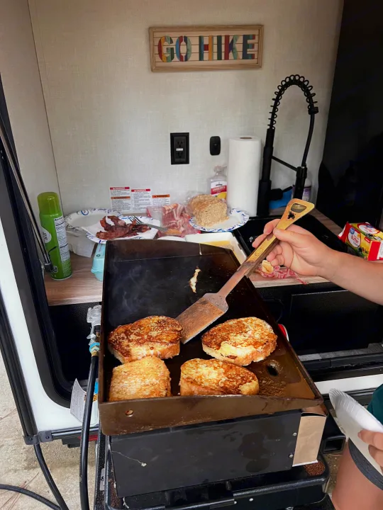 Cooking French toast and bacon on a griddle in an RV rental's outdoor kitchen. A perfect camping breakfast.. Forest River NoBo 10.7 2024